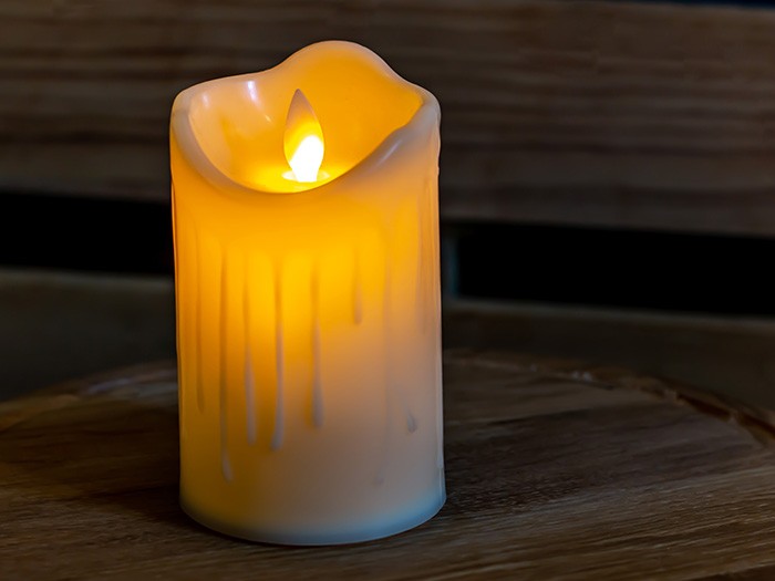 Flameless white candle with dim yellow light on a wooden table. 